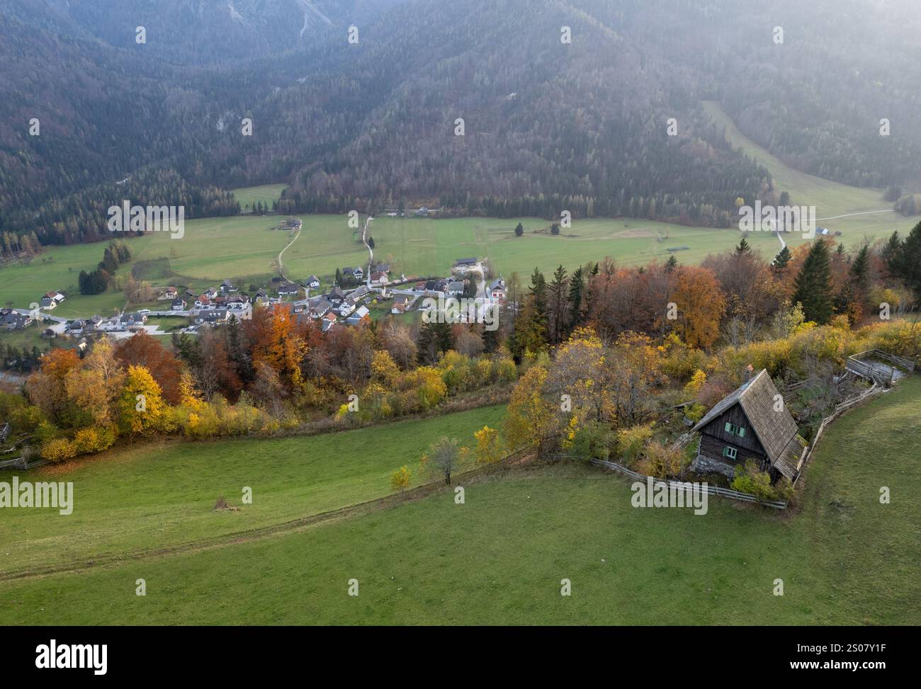 Drone Vista aerea di un pittoresco villaggio e di una solitaria cabina di legno annidata nel vibrante fogliame autunnale delle alpi Foto Stock