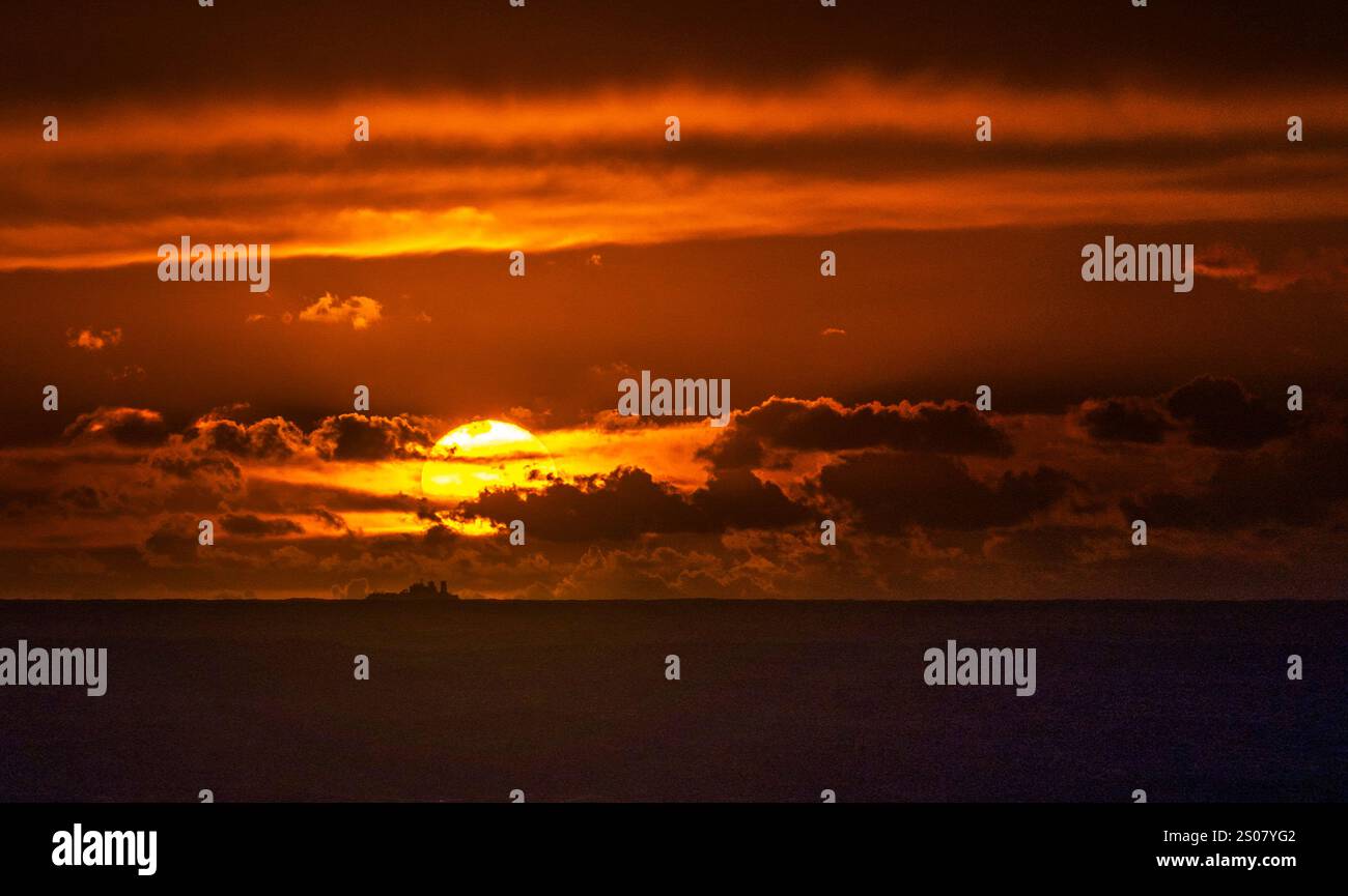 Un tramonto spettacolare sull'oceano, con vivaci sfumature arancioni e gialle che illuminano il cielo. Le nuvole scure sono sparse, creando un contrasto sorprendente Foto Stock