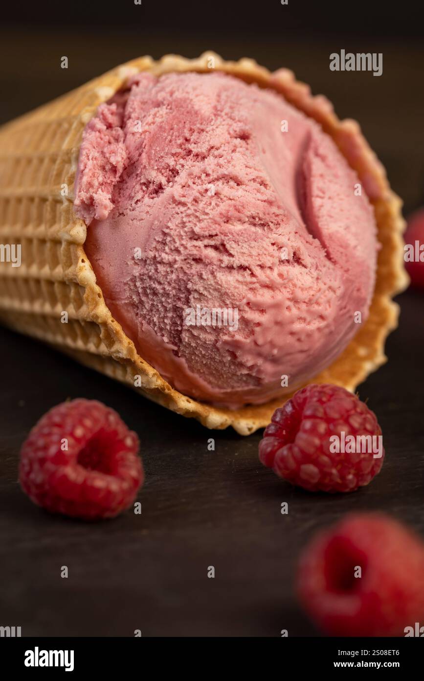 gelato al lampone rosso in un cono per waffle su sfondo nero, delizioso gelato freddo al lampone e lamponi maturi Foto Stock