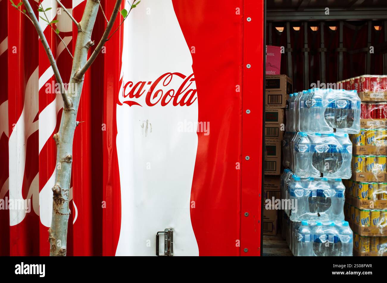 Immagine editoriale di un camion di consegna Coca-Cola in un ambiente urbano, con il suo iconico marchio rosso e bianco. Pile di acqua in bottiglia e pacchi di bibite gassate Foto Stock