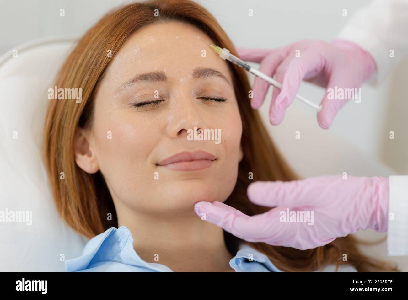 Il cliente si siede comodamente in una clinica luminosa, sorridendo come un professionista applica il trattamento di filler dermico. L'atmosfera serena favorisce il relax e la Foto Stock