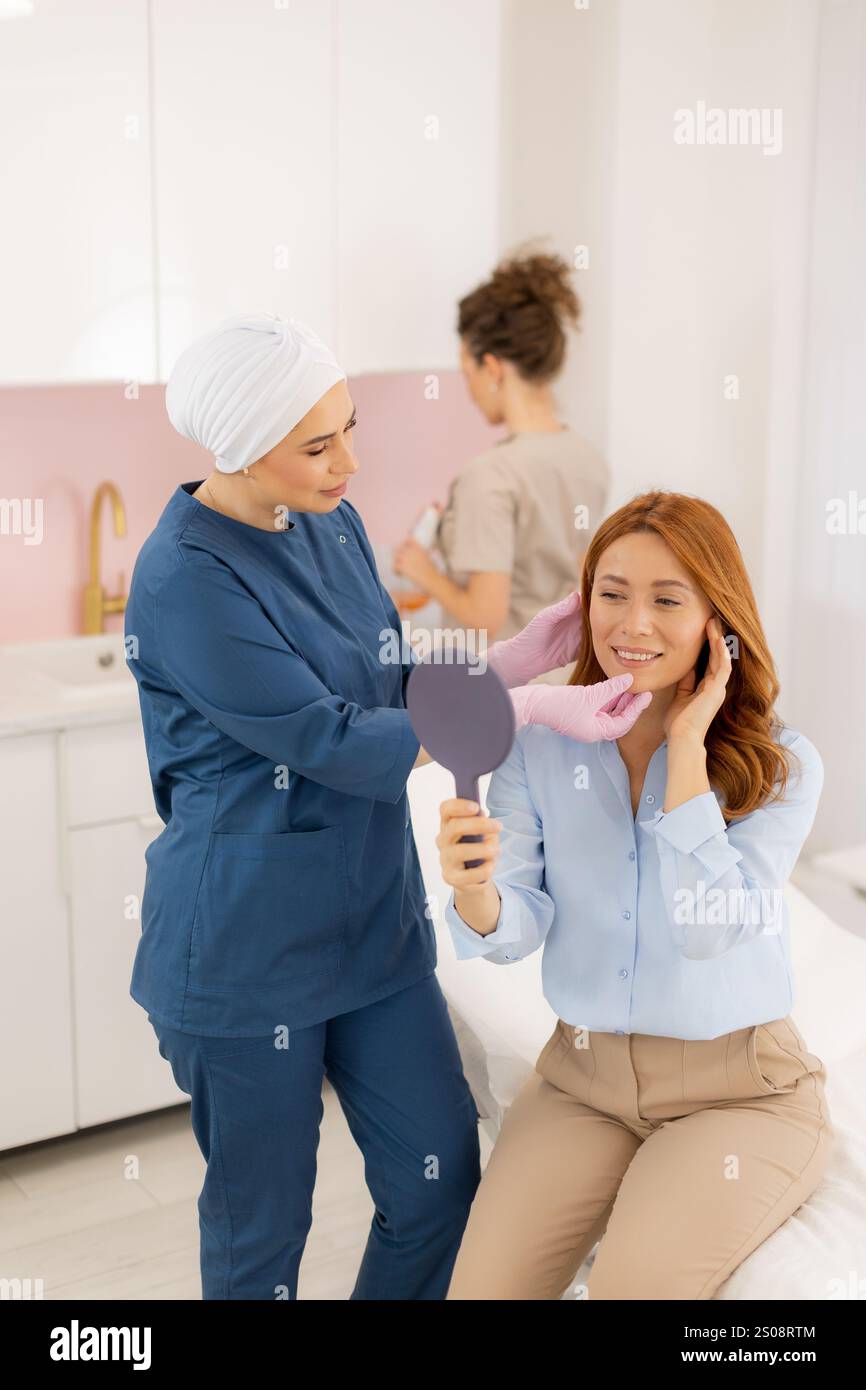 Un estetista esperto fornisce una consulenza personalizzata per la cura della pelle, acconciando delicatamente i capelli del cliente mentre ammira il suo riflesso radioso. Naturale l Foto Stock