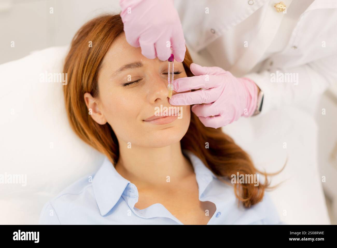 Una donna gode di una rinfrescante procedura per la cura della pelle, giacendo comodamente mentre un professionista esperto applica siero nutriente. L'atmosfera è rilassante, promo Foto Stock