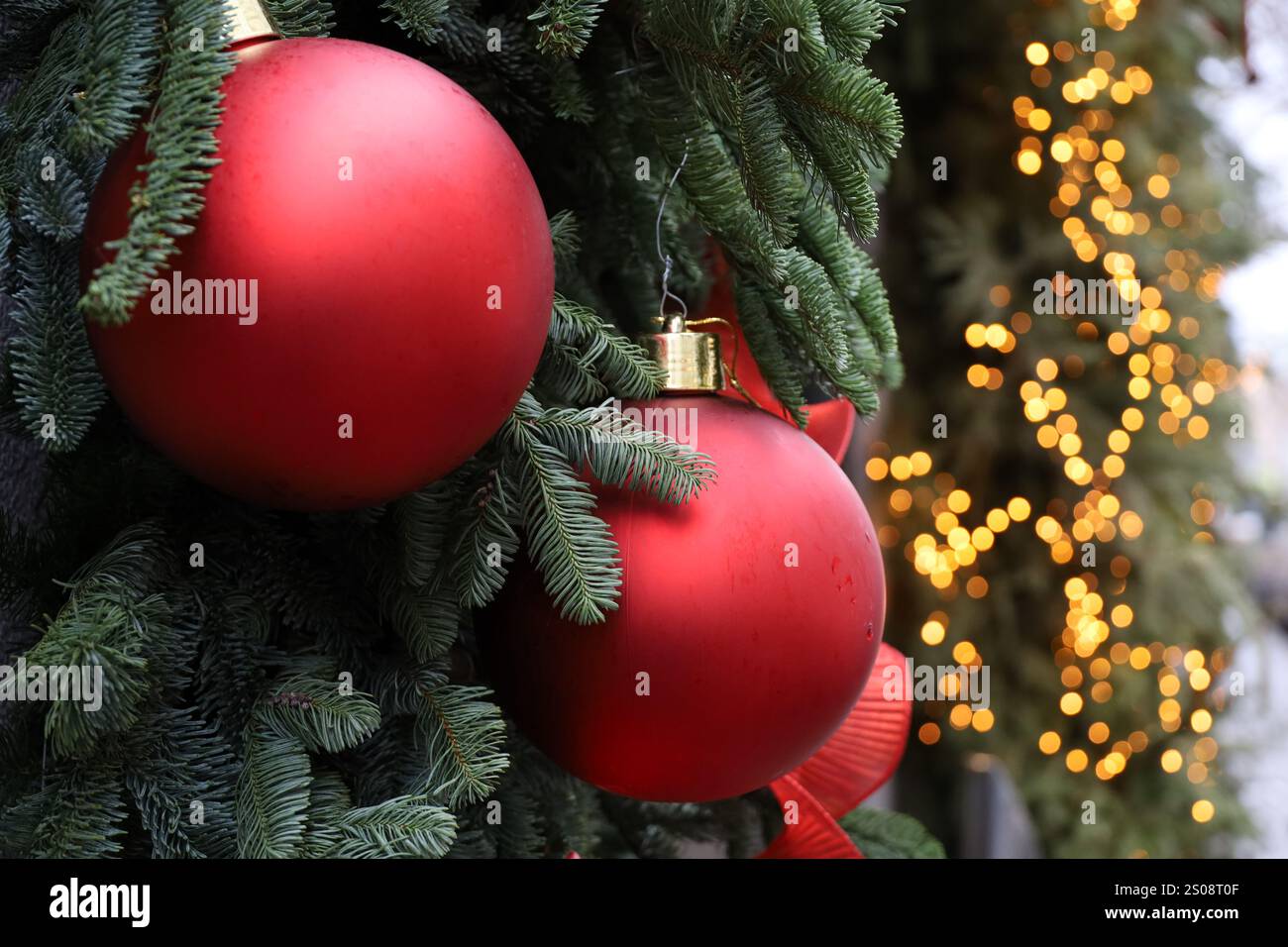 Festa di Capodanno nella città invernale, rami di alberi di Natale con palle rosse sullo sfondo delle luci dorate Foto Stock