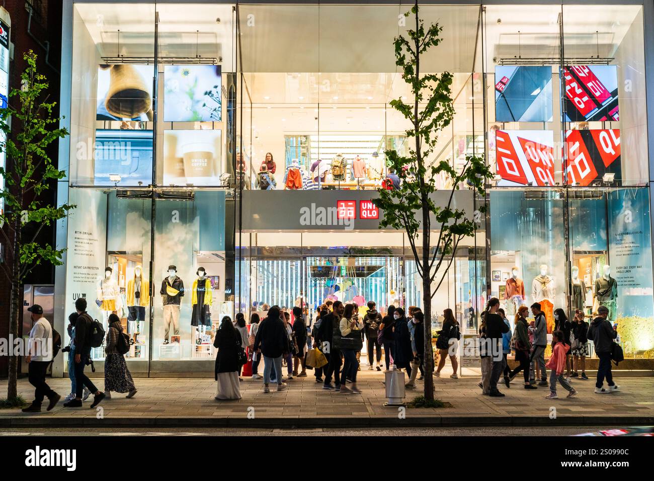 La facciata e l'ingresso dei primi due piani del flagship store uni Qlo sulla Ginza di notte. Marciapiede all'aperto affollato di amanti dello shopping. Foto Stock
