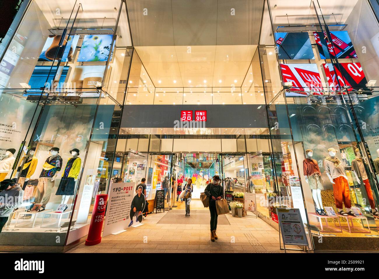 La facciata e l'ingresso dei primi due piani del flagship store uni Qlo sulla Ginza di notte. Marciapiede all'aperto affollato di amanti dello shopping. Foto Stock
