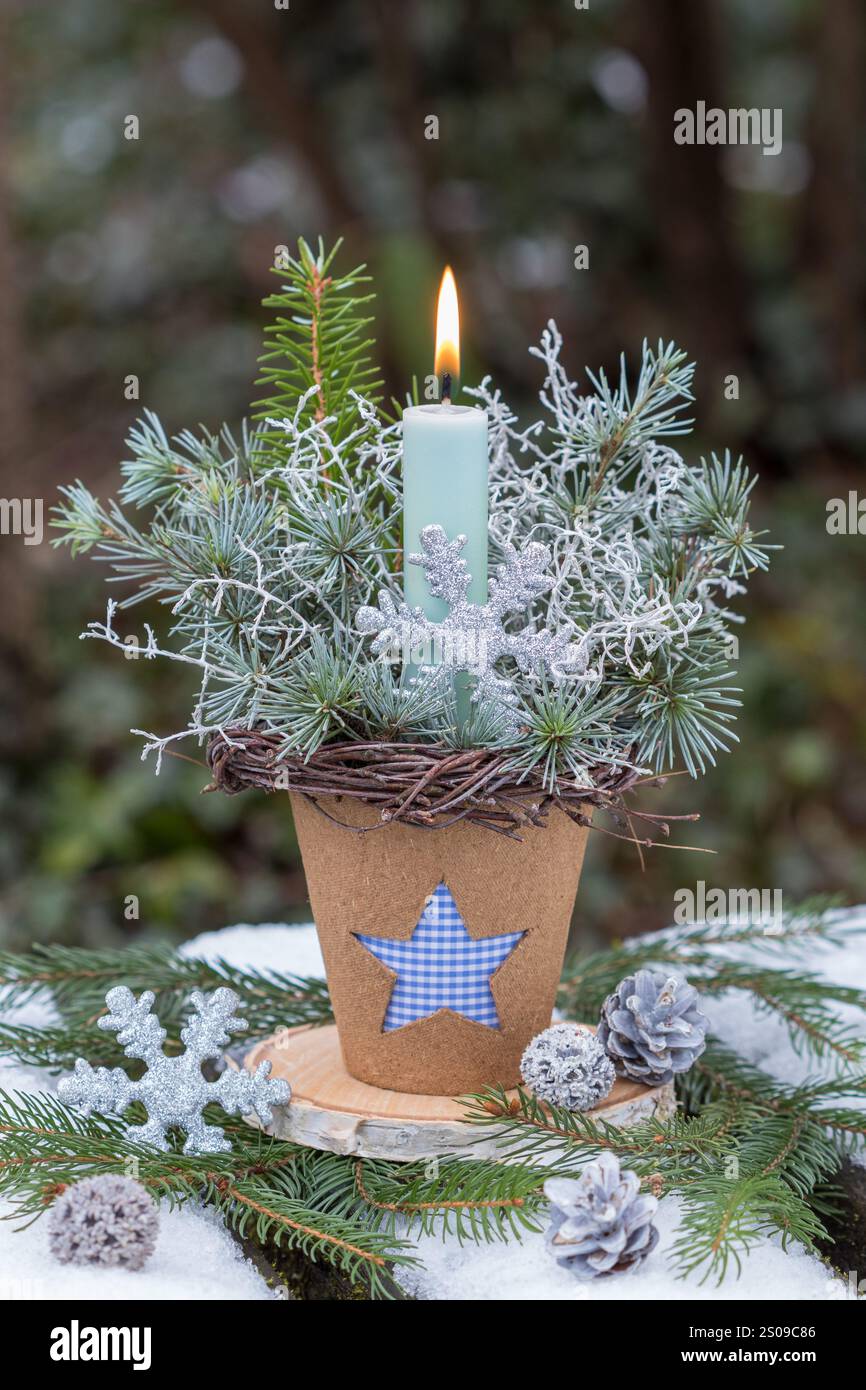 accordo natalizio con candela, rami di pino, filo spinato e fiocco di neve in una pentola di torba con ornamento a stella Foto Stock