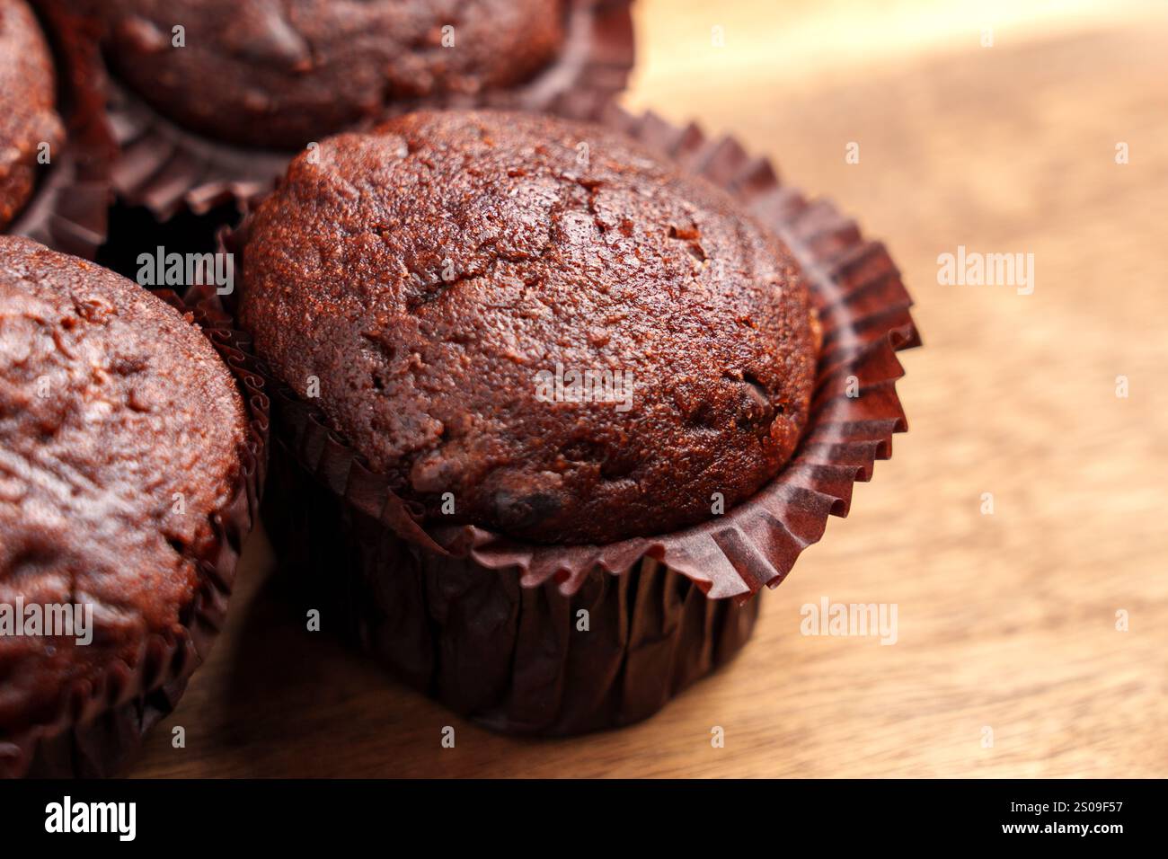 Muffin al cioccolato appena sfornati in involtini di carta marrone su una superficie di legno. Concetto di dolcetti fatti in casa e dolcezza Foto Stock