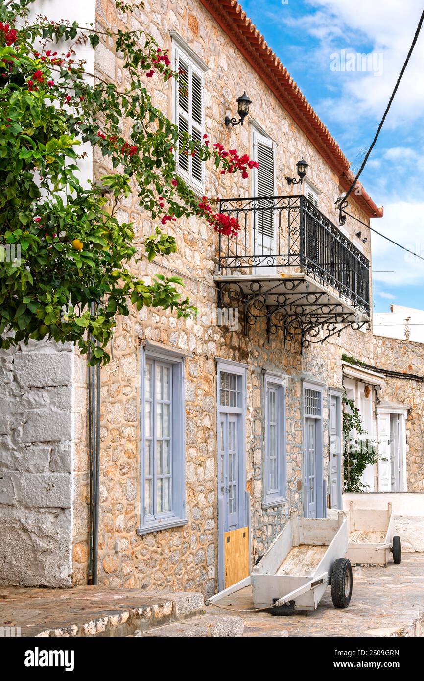Un pittoresco edificio in pietra con balcone su uno stretto vicolo pieno di fiori nel villaggio sul mare di Hydra, sull'isola di Hydra, in Grecia. Foto Stock