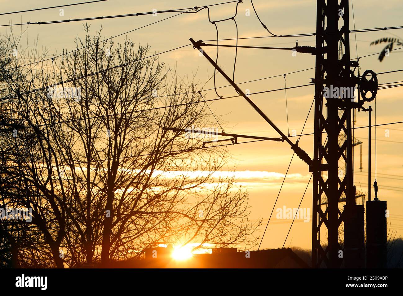 Fahrleitungen für den Bahnstrom Fahrleitungen der Deutschen Bahn befindet sich von Masten und Auslegern gehalten über einer Eisenbahnlinie, während im Hintergrund die Sonne untergeht. *** Le linee aeree per la corrente di trazione le linee aeree della Deutsche Bahn sono tenute da alberi e bracci sopra una linea ferroviaria mentre il sole tramonta sullo sfondo Foto Stock