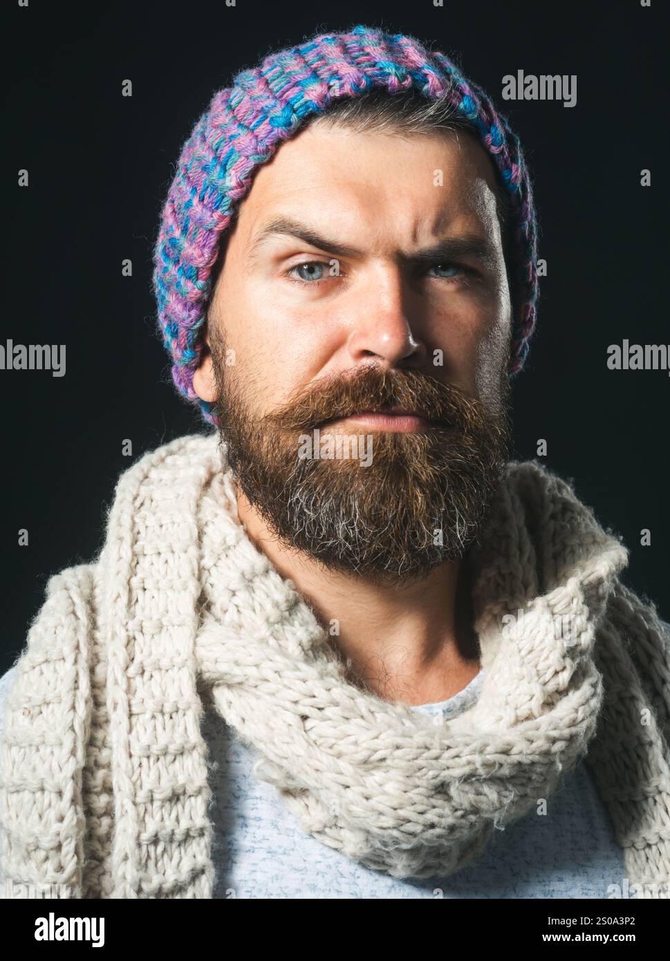 La moda invernale degli uomini. Uomo barbuto in cappello di lana, sciarpa e maglione. Uomo attraente con barba e baffi in abiti caldi. Un tipo serio alla moda Foto Stock