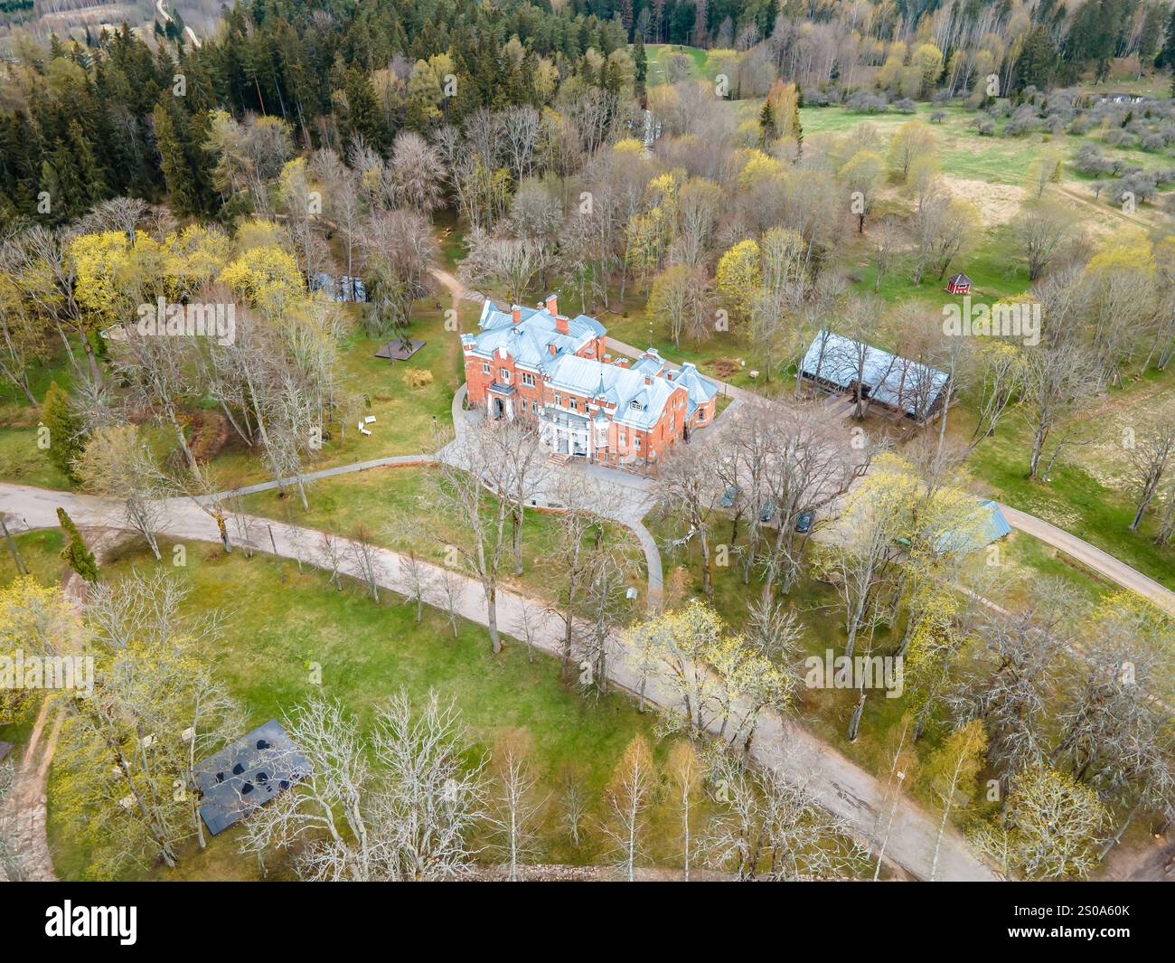 Una prospettiva aerea cattura una grande villa in mattoni dal design simmetrico, circondata da alberi decidui e conifere, aree erbose aperte e nea Foto Stock