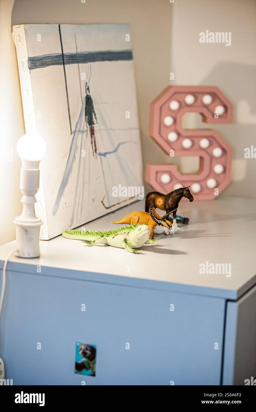Un angolo della camera presenta un armadio bianco con una lampada, un paesaggio innevato dipinto, una lettera S illuminata e animali giocattolo, creando un'atmosfera giocosa. Foto Stock