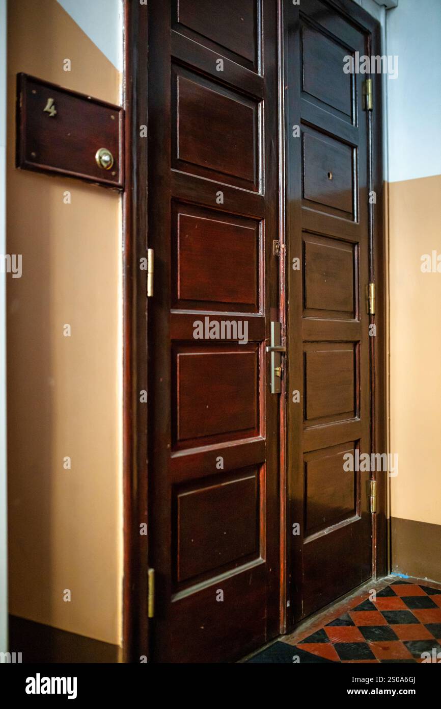Una porta di legno scuro con maniglia in ottone e spioncino si erge in un corridoio con pareti beige. Una targa con il numero 4 è accanto ad essa, sopra una t a scacchi Foto Stock