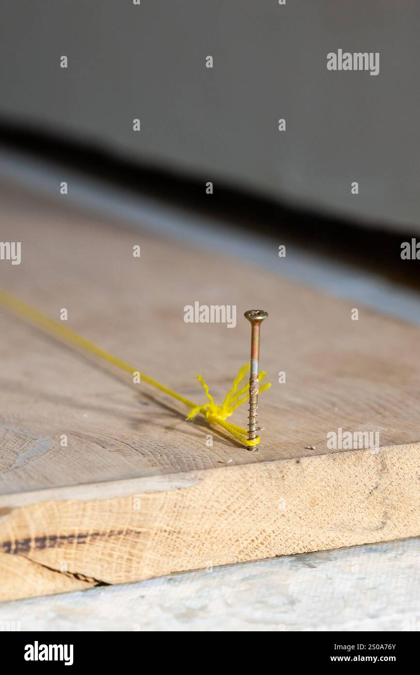 Una tavola in legno è dotata di una vite parzialmente azionata con una corda gialla tesa avvolta intorno ad essa, inserita in un ambiente di costruzione interno o di falegnameria. Foto Stock