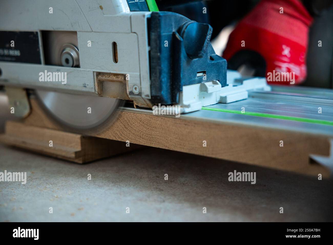 Una sega circolare taglia il legno su una guida azionata da una persona con guanti rossi. L'attenzione si concentra sulla precisione della lama e sull'azione dinamica di Foto Stock