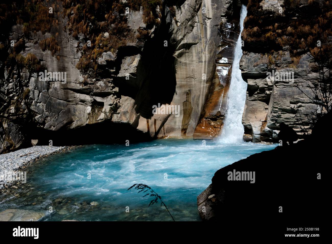 Uomo sagomato sulla scogliera sopra una piscina di cascata che scorre nel fiume Nilgiri, Annapurna North base Camp Trek, Nepal Foto Stock