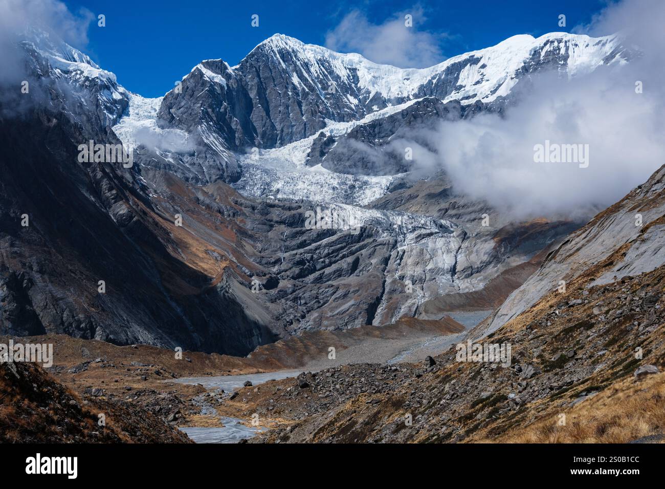I ghiacciai precipitano giù per la ripida parete nord del Nilgiri vicino al campo base nord dell'Annapurna e nutrono un piccolo ruscello in primo piano Foto Stock