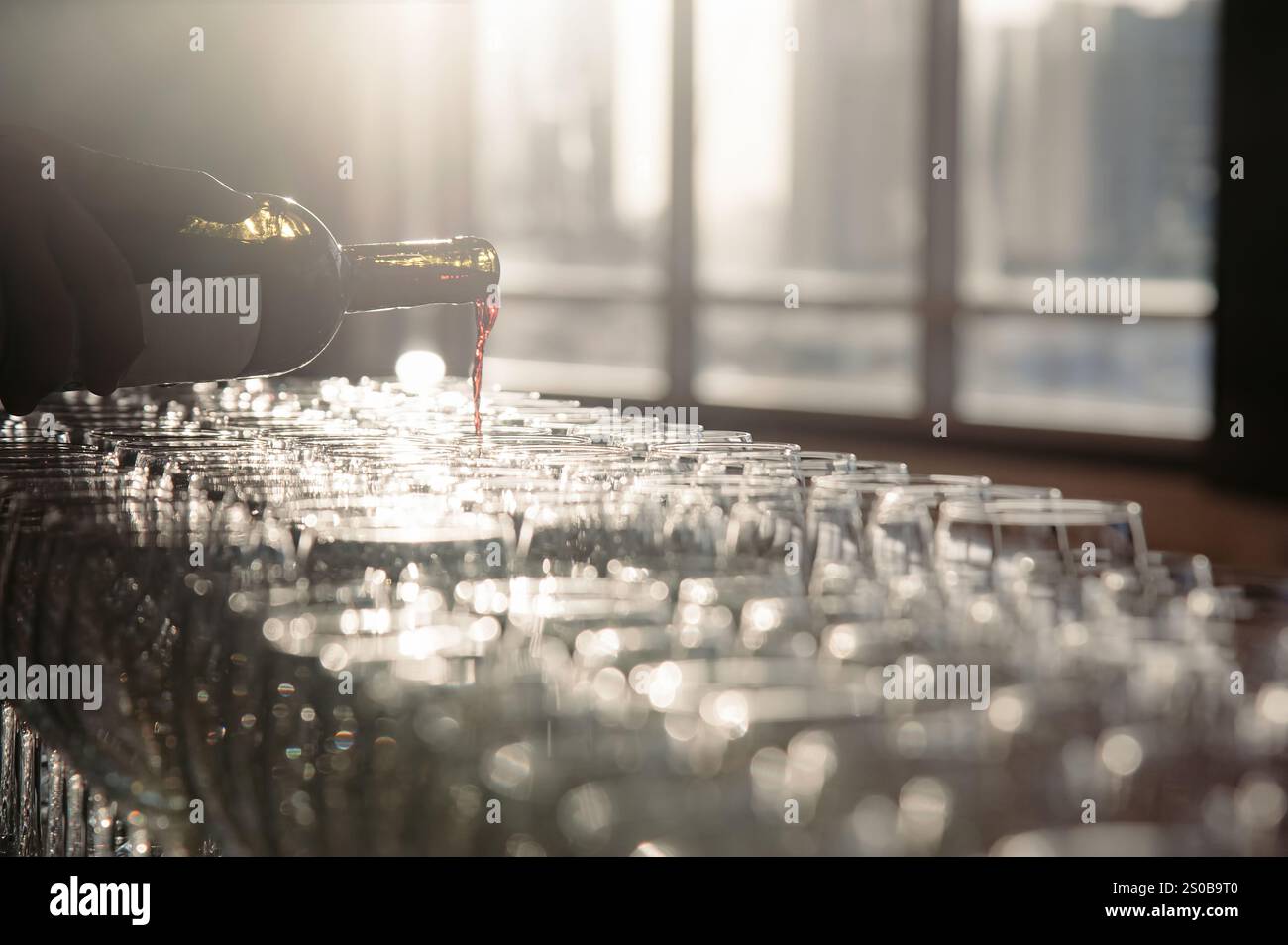 un cameriere che versa vino rosso dalla bottiglia all'eneglass, che ha dato il benvenuto alla cena in serata. la foto ha un effetto flare dalla retroilluminazione Foto Stock
