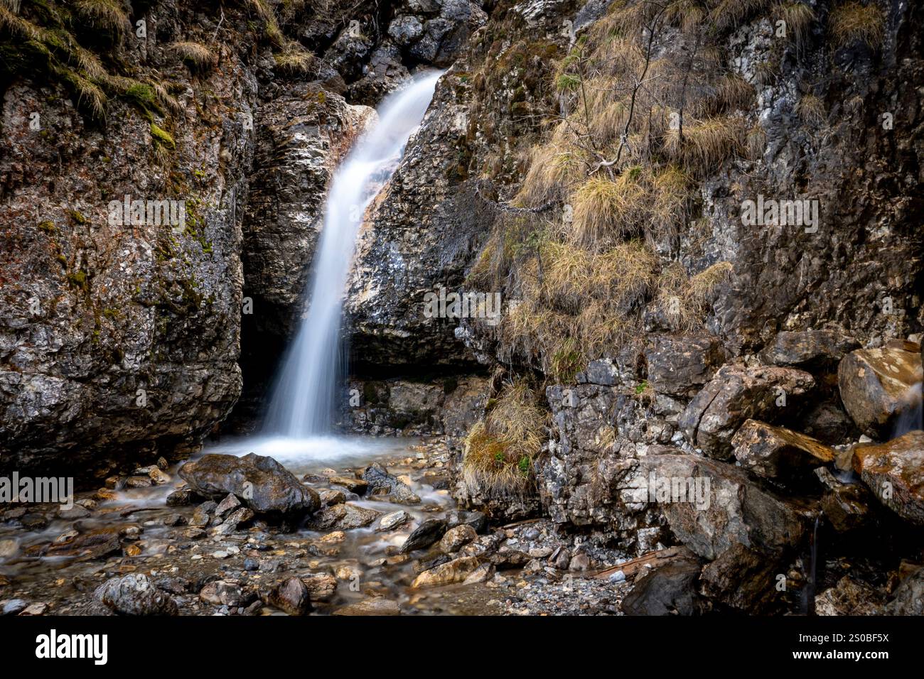 Una cascata serena scende lungo una scogliera rocciosa circondata da muschio e vegetazione. Foto Stock