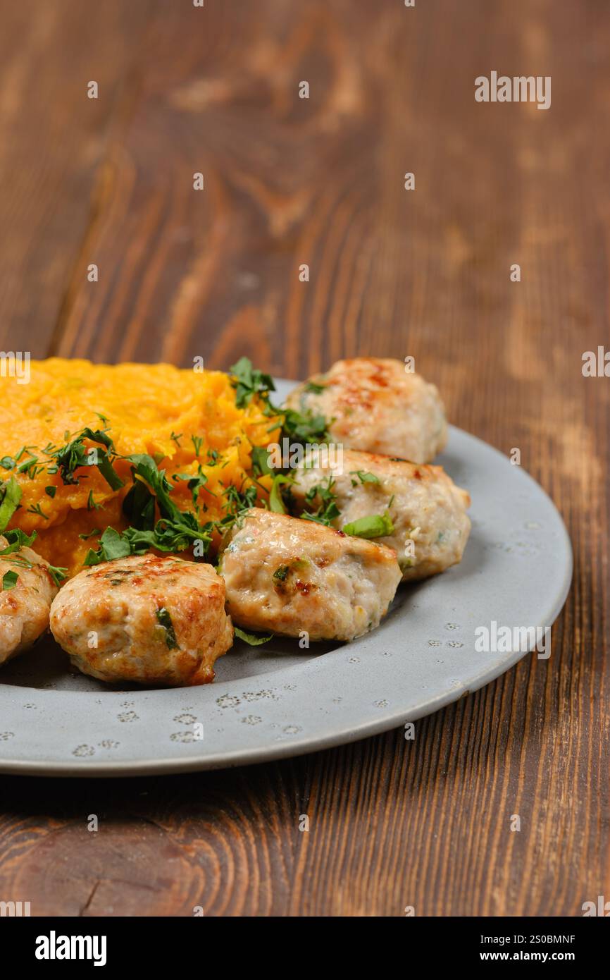 Vista ravvicinata di un piatto con polpette appena preparate guarnite con erbe e una porzione di zucca schiacciata liscia e cremosa Foto Stock