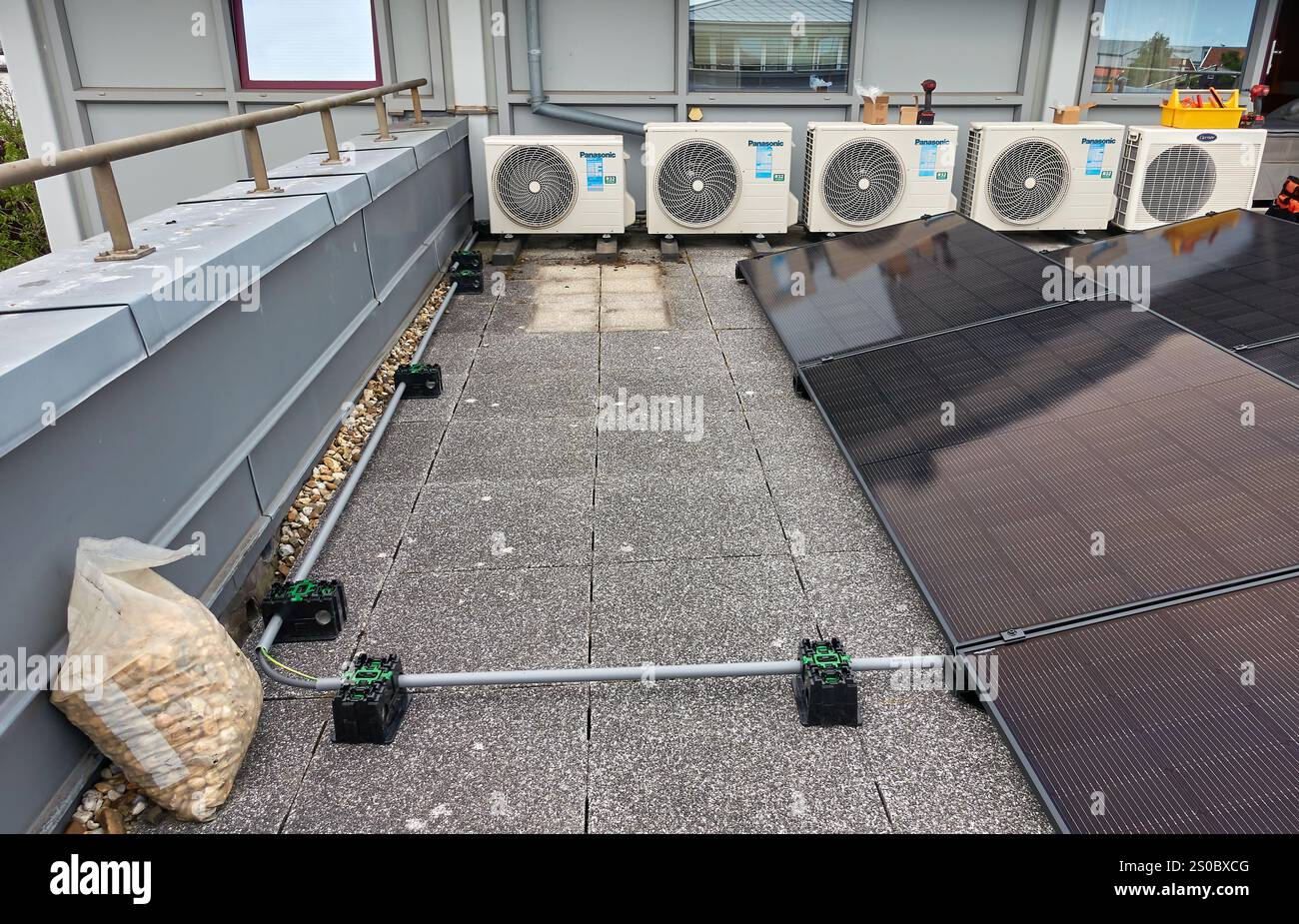 Un sistema compatto di pannelli solari per terrazze sul tetto con unità HVAC sullo sfondo, che mette in mostra la tecnologia dell'energia pulita in un ambiente urbano moderno nel ne Foto Stock