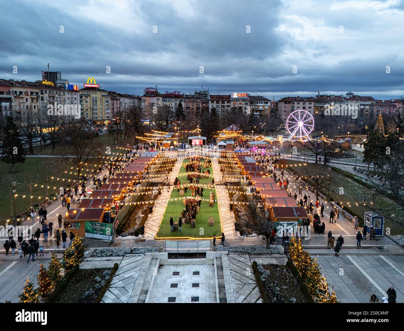 Un'affascinante vista aerea del mercato di Natale di Sofia al crepuscolo, vicino a NDK, con luci vivaci, bancarelle festose, una ruota panoramica, e festeggiamenti natalizi. Foto Stock