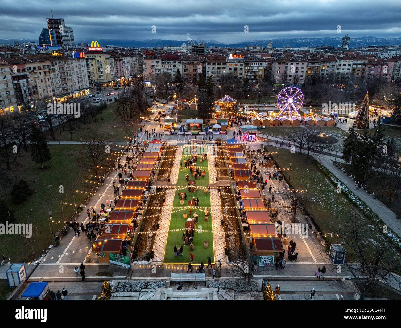 Un'affascinante vista aerea del mercato di Natale di Sofia al crepuscolo, vicino a NDK, con luci vivaci, bancarelle festose, una ruota panoramica, e festeggiamenti natalizi. Foto Stock
