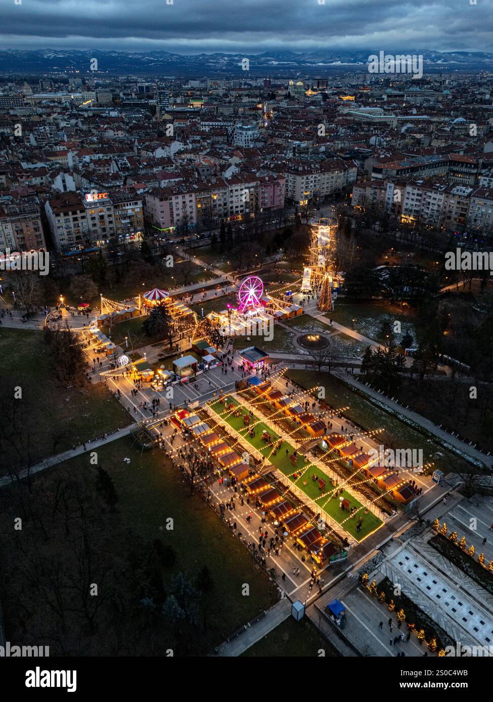 Un'affascinante vista aerea del mercato di Natale di Sofia al crepuscolo, vicino a NDK, con luci vivaci, bancarelle festose, una ruota panoramica, e festeggiamenti natalizi. Foto Stock