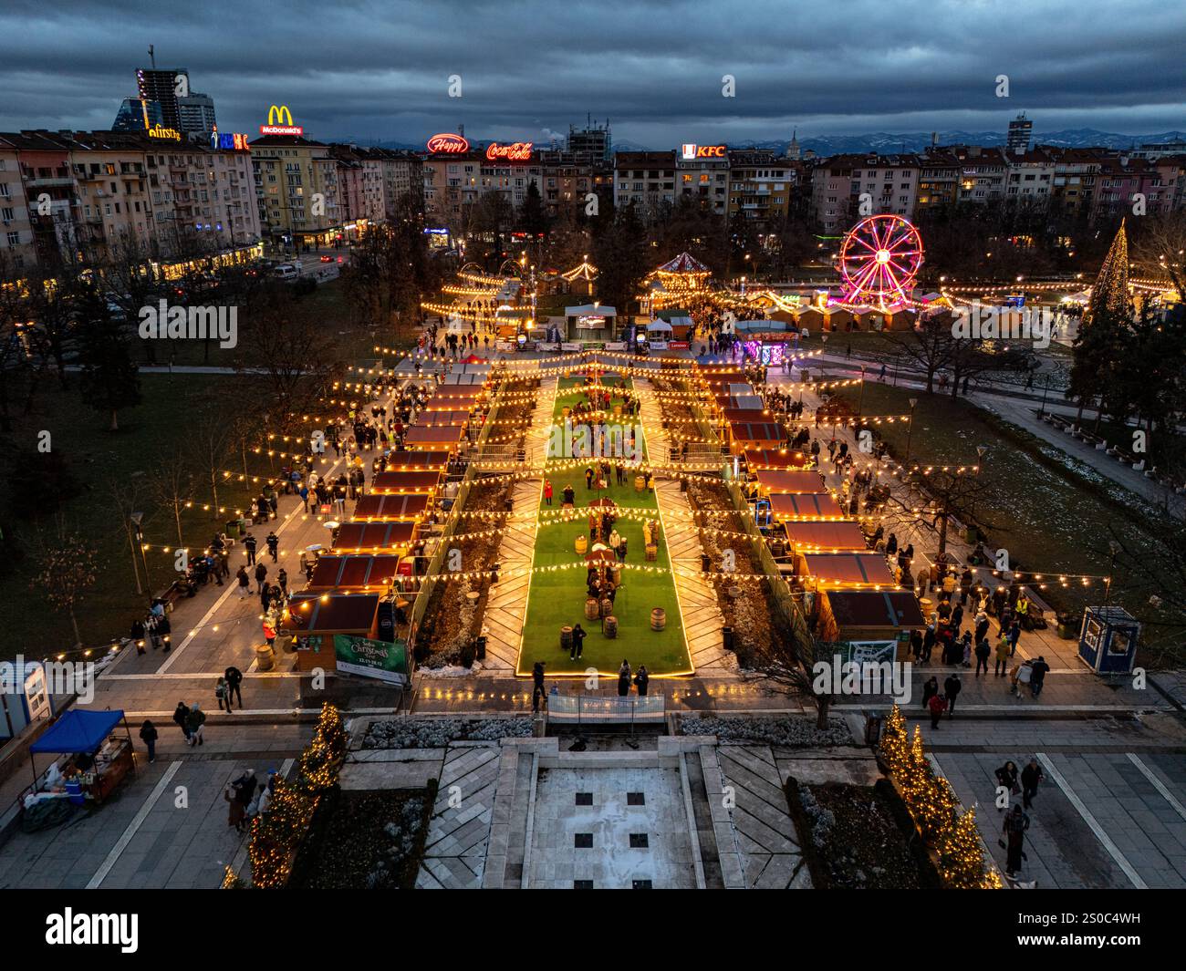 Un'affascinante vista aerea del mercato di Natale di Sofia al crepuscolo, vicino a NDK, con luci vivaci, bancarelle festose, una ruota panoramica, e festeggiamenti natalizi. Foto Stock