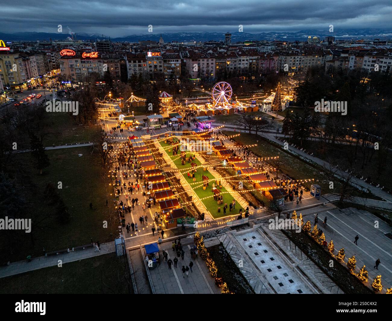 Un'affascinante vista aerea del mercato di Natale di Sofia al crepuscolo, vicino a NDK, con luci vivaci, bancarelle festose, una ruota panoramica, e festeggiamenti natalizi. Foto Stock