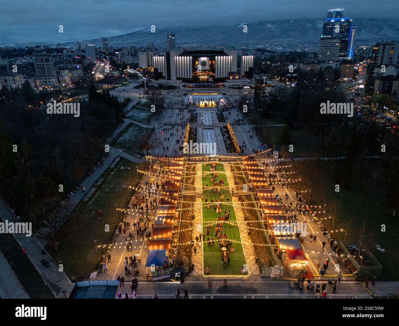 Vista aerea notturna del Palazzo Nazionale della Cultura (NDK) di Sofia, Bulgaria, con bancarelle illuminate per il mercato di Natale, vivaci luci della città, e. Foto Stock