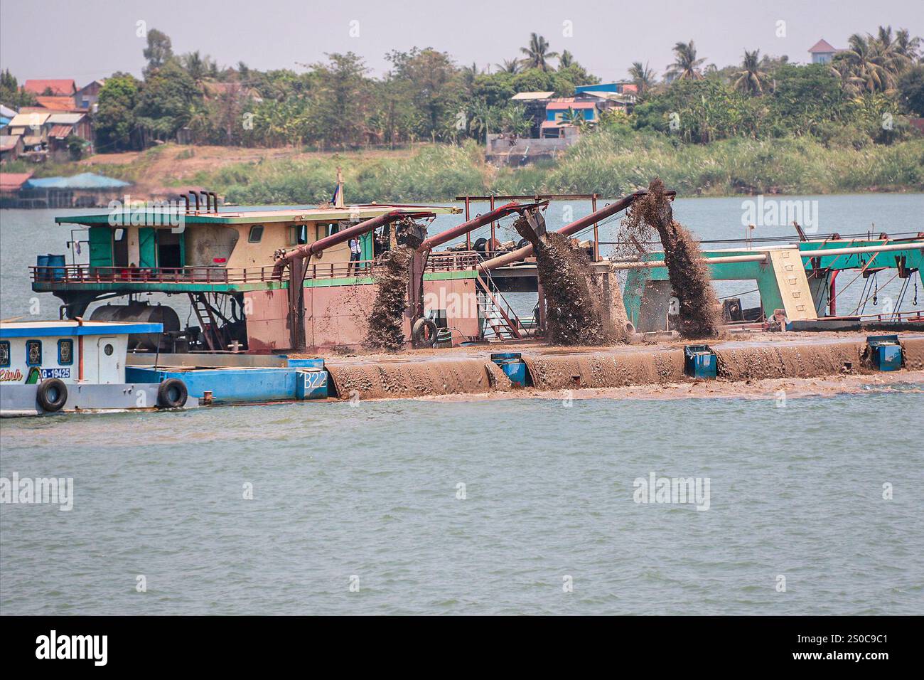 Mekong Delta, Vietnam. 27 dicembre 2024: Piattaforma di dragaggio draga il canale e carica navi/chiatte da carico. L'estrazione di sabbia e ghiaia (miniere o draghe) utilizzata per il calcestruzzo nell'industria edile solleva avvertenze circa l'impatto ambientale del sovrasfruttamento dei sedimenti del letto dei fiumi (biodiversità ed ecosistema), ma anche sulla vita delle persone che vivono sulle rive dei fiumi. Lo sfruttamento legale o illegale della sabbia provoca una massiccia erosione delle banche, con conseguente perdita di terreni agricoli, ma anche il crollo di edifici e case e lo spostamento delle popolazioni. Crediti: KEVIN IZORCE/Alamy Live News Foto Stock