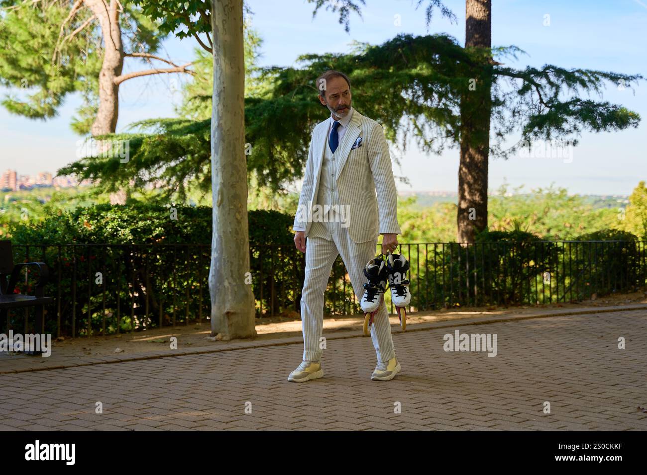 Uomo caucasico di oltre 50 anni in tuta a a righe che tiene pattini a rotelle in un parco soleggiato Foto Stock