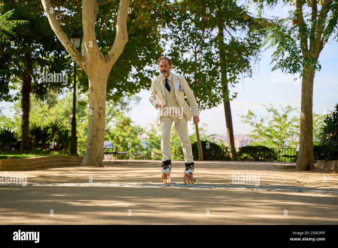 Uomo con una tuta beige e cimentarsi in un parco soleggiato, circondato da lussureggianti alberi verdi e paesaggi urbani sullo sfondo. Foto Stock