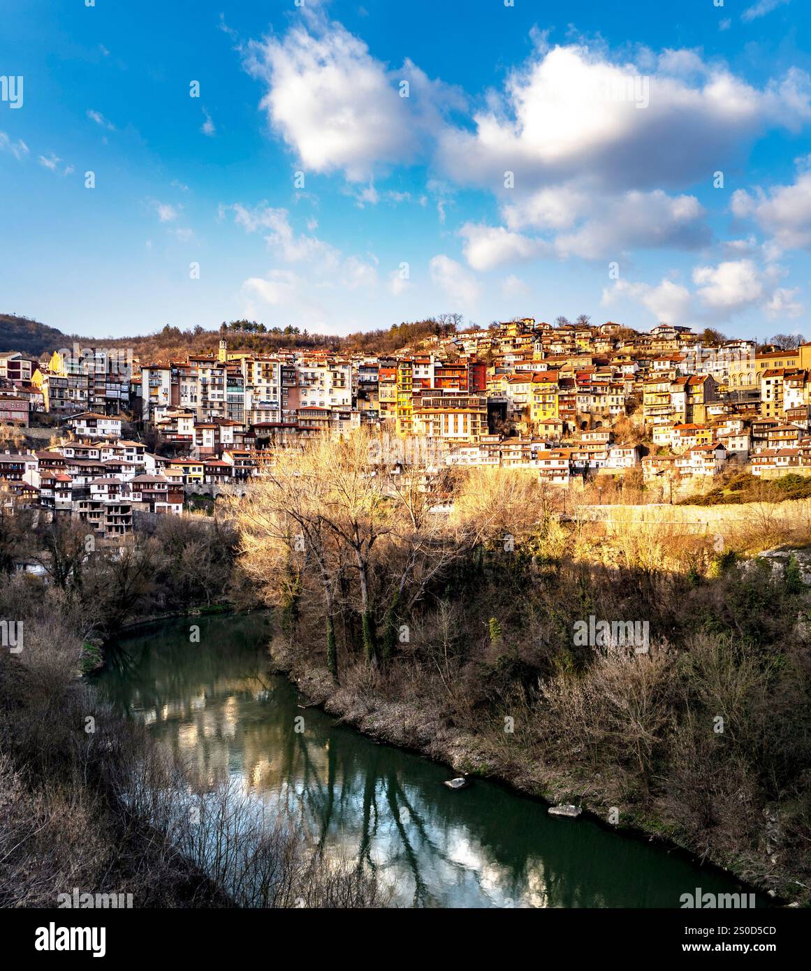 Una vista pittoresca di una città storica con edifici colorati su una collina, che si affaccia su un fiume calmo con riflessi del cielo e delle nuvole. Lo scen Foto Stock