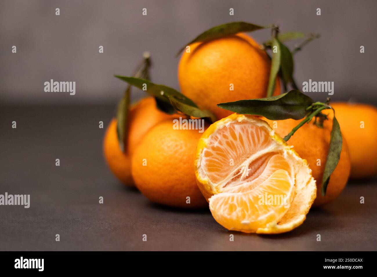 Un mandarino sbucciato e un mandarino intero con foglie su sfondo grigio Foto Stock