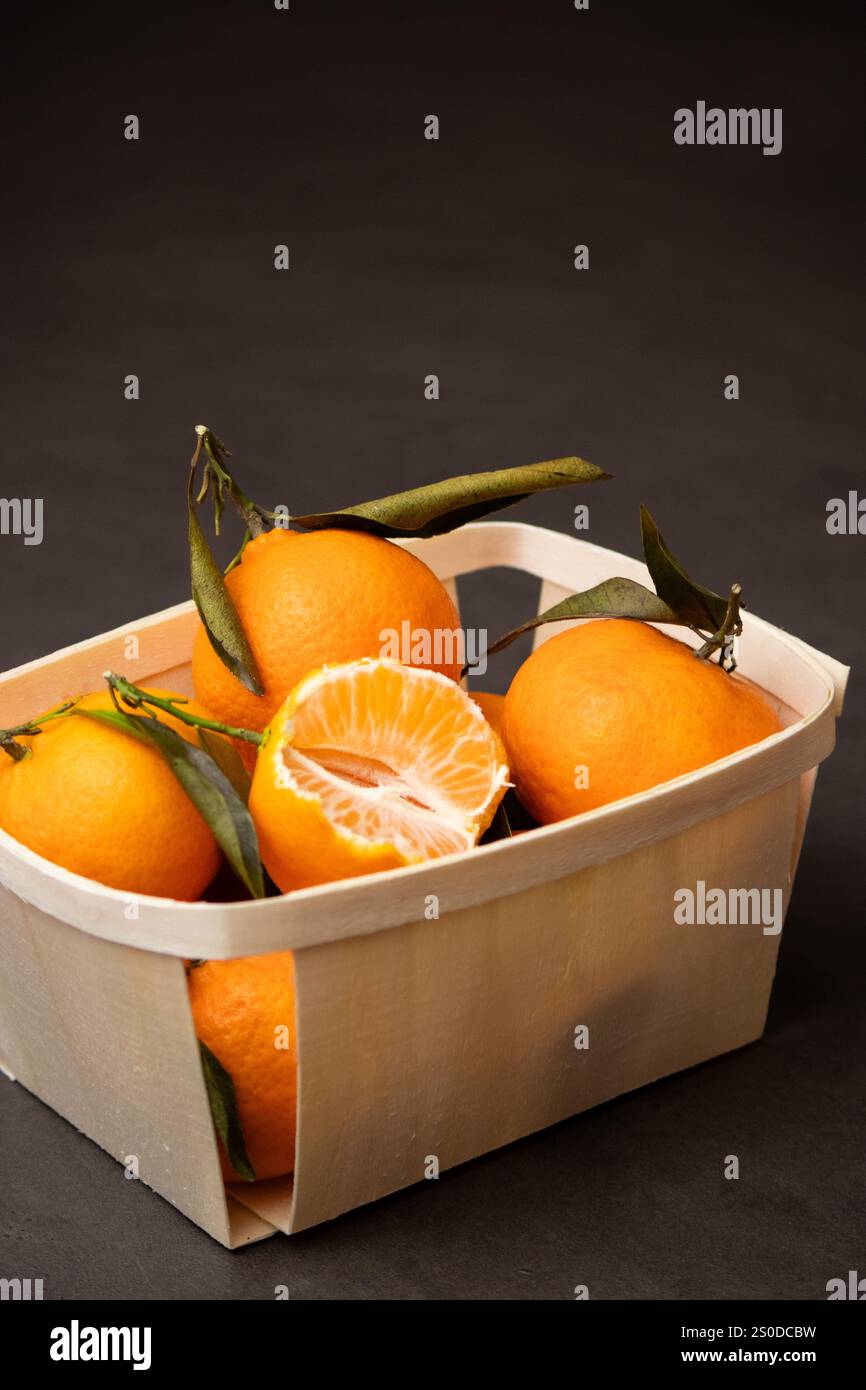 Primo piano di mandarini interi e un frutto pelato in una scatola di legno su sfondo grigio Foto Stock
