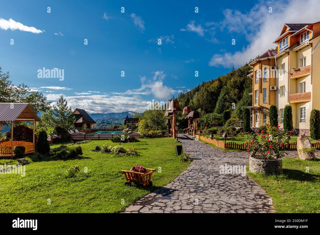 Un bellissimo giardino con un sentiero in pietra che conduce ad un edificio. Il giardino è pieno di fiori e piante, e c'è un piccolo carro di legno nel mezzo Foto Stock