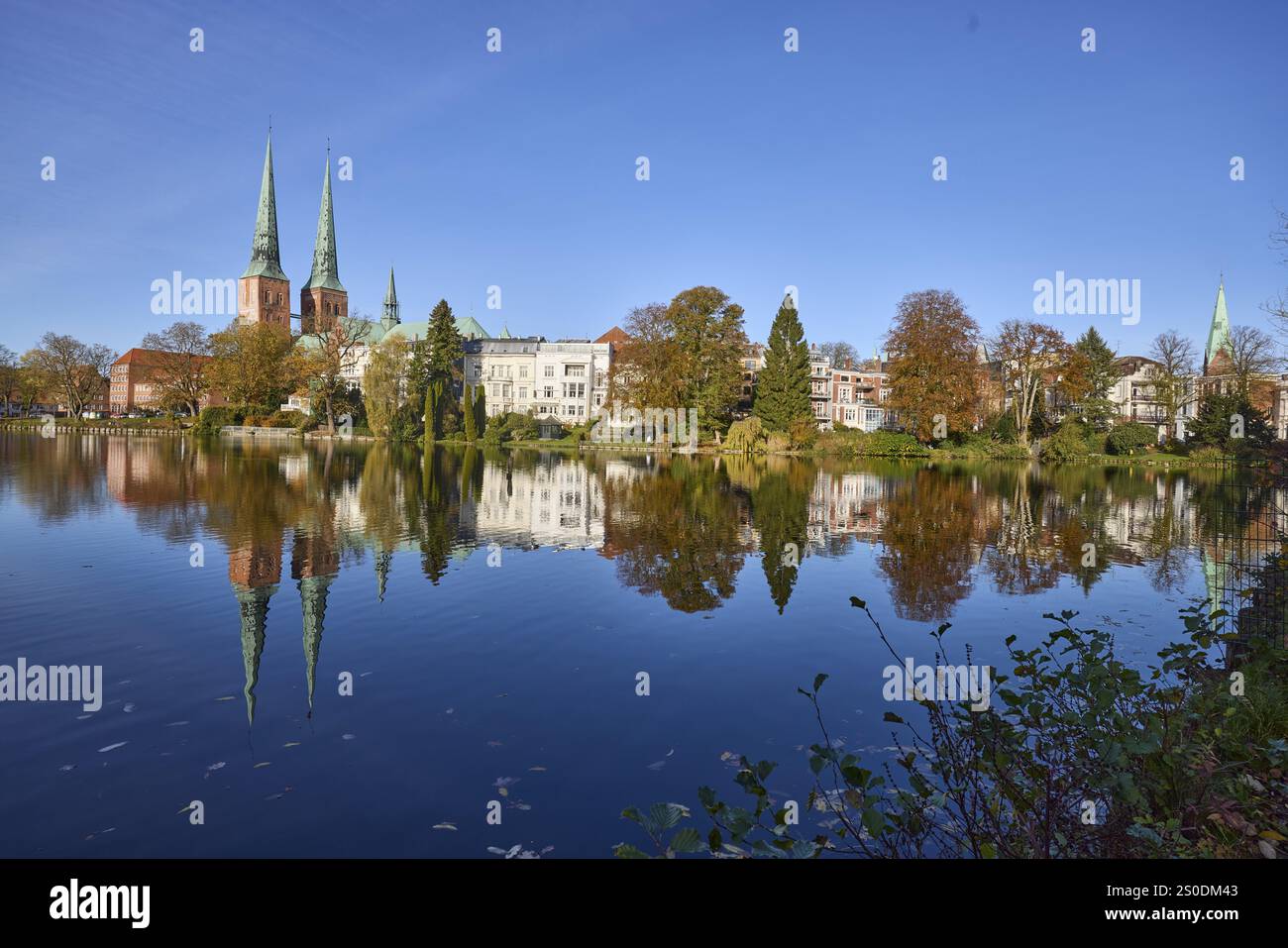 Laghetto con edifici generali, cattedrale di Lubecca e alberi, riflessi simmetrici sulla superficie dell'acqua, cielo azzurro senza nuvole, città anseatica di Lue Foto Stock