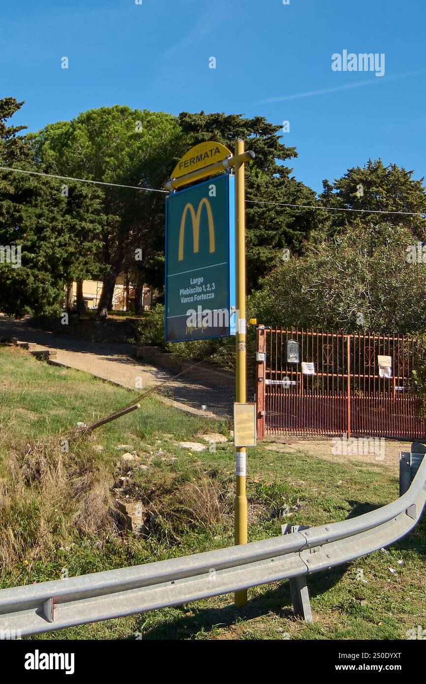 Civitavecchia, Italia - 27 dicembre 2024: Segnale di fermata dell'autobus con logo McDonald's e località, in zona rurale con vegetazione. Ringhiera in metallo e porta rossa Foto Stock