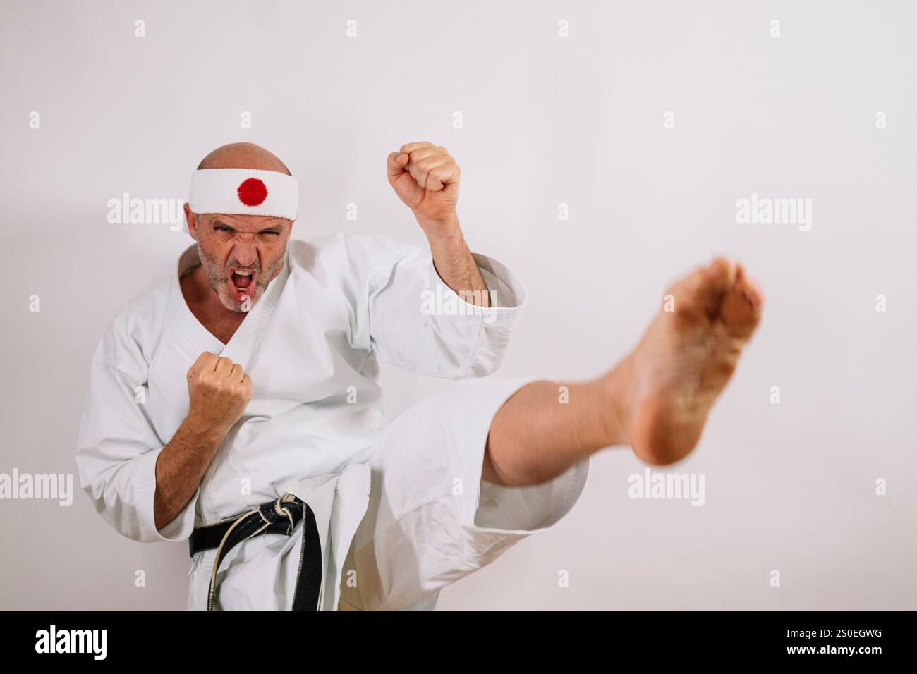 Karateka senior che esegue un calcio potente, una concentrazione intensa. Foto Stock