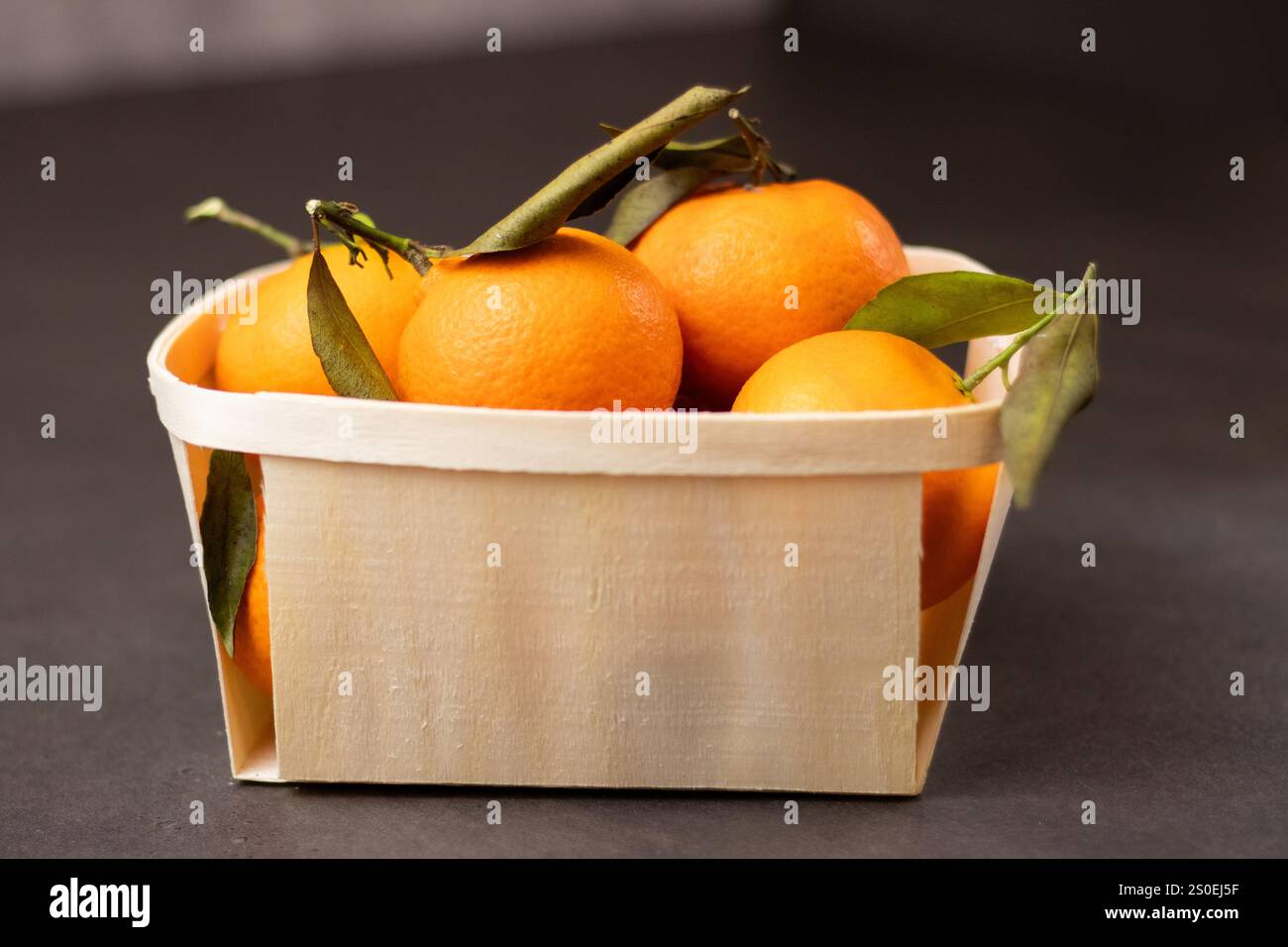 Primo piano di frutta mandarina in una scatola di legno su sfondo grigio Foto Stock