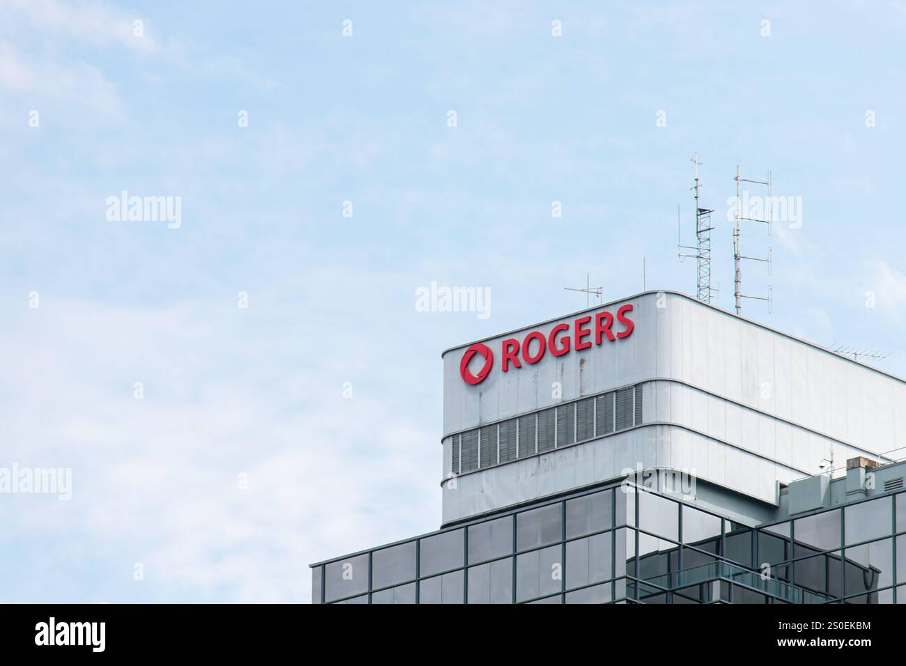 Burnaby, CANADA - 2 agosto 2024 : cima di un edificio Rogers con antenne di comunicazione e un importante logo rosso, adagiato su un cielo azzurro. Foto Stock