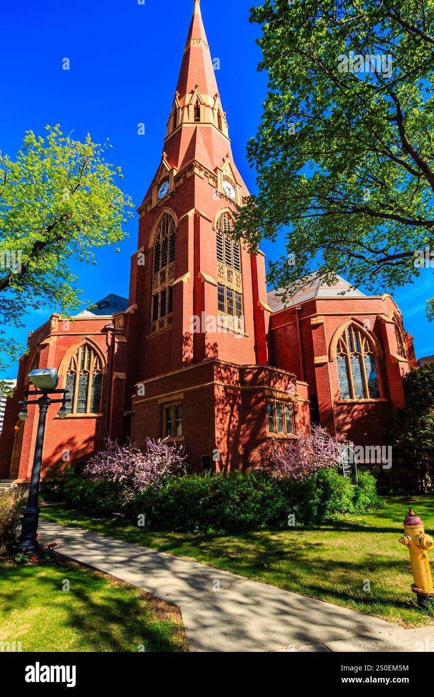 Una grande chiesa in mattoni rossi con un campanile e una croce in cima. La chiesa è circondata da alberi e ha un idrante giallo nell'erba Foto Stock