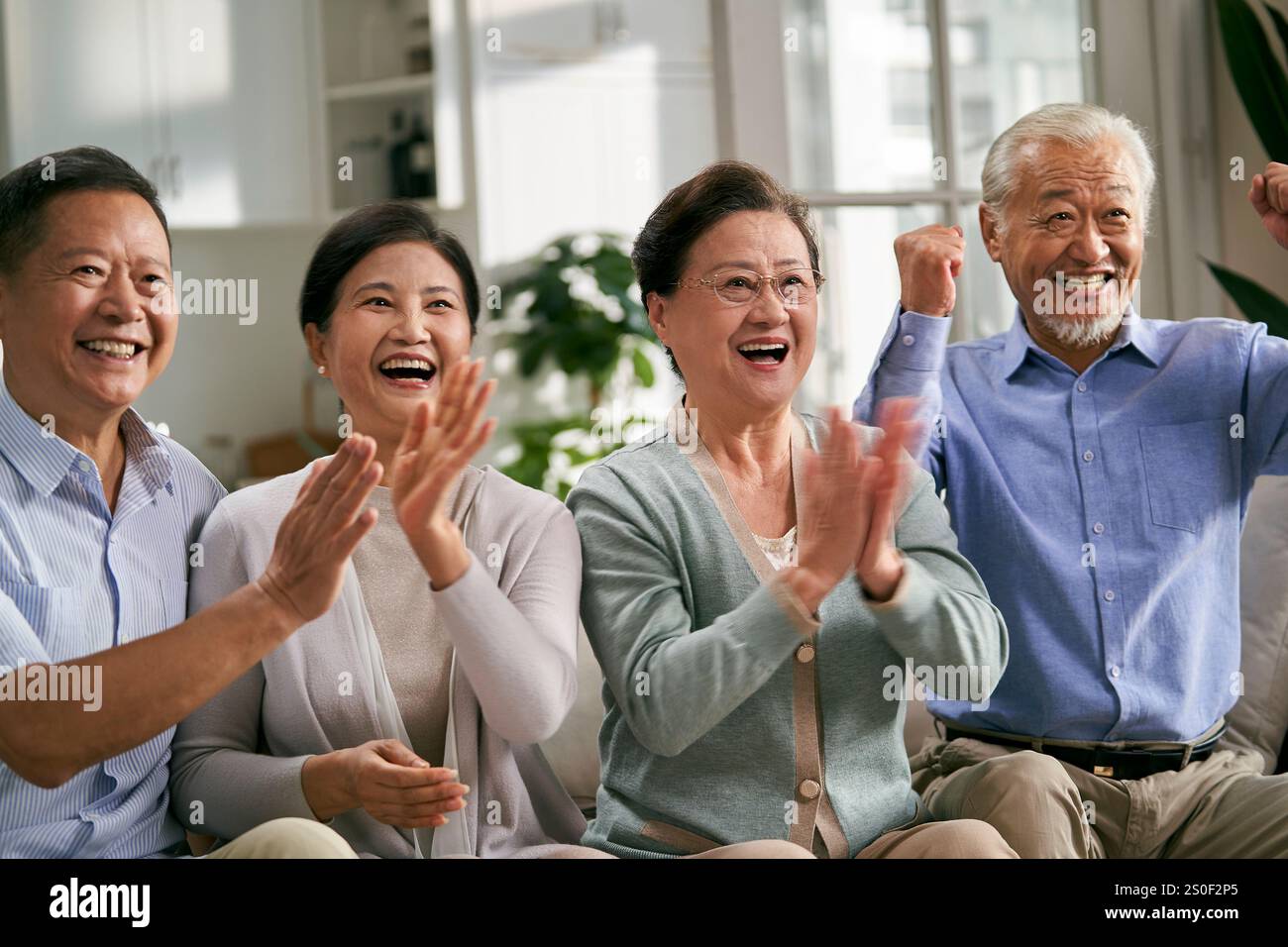 Due coppie asiatiche senior felici sedute sul divano a casa a guardare una partita di sport in TV Foto Stock