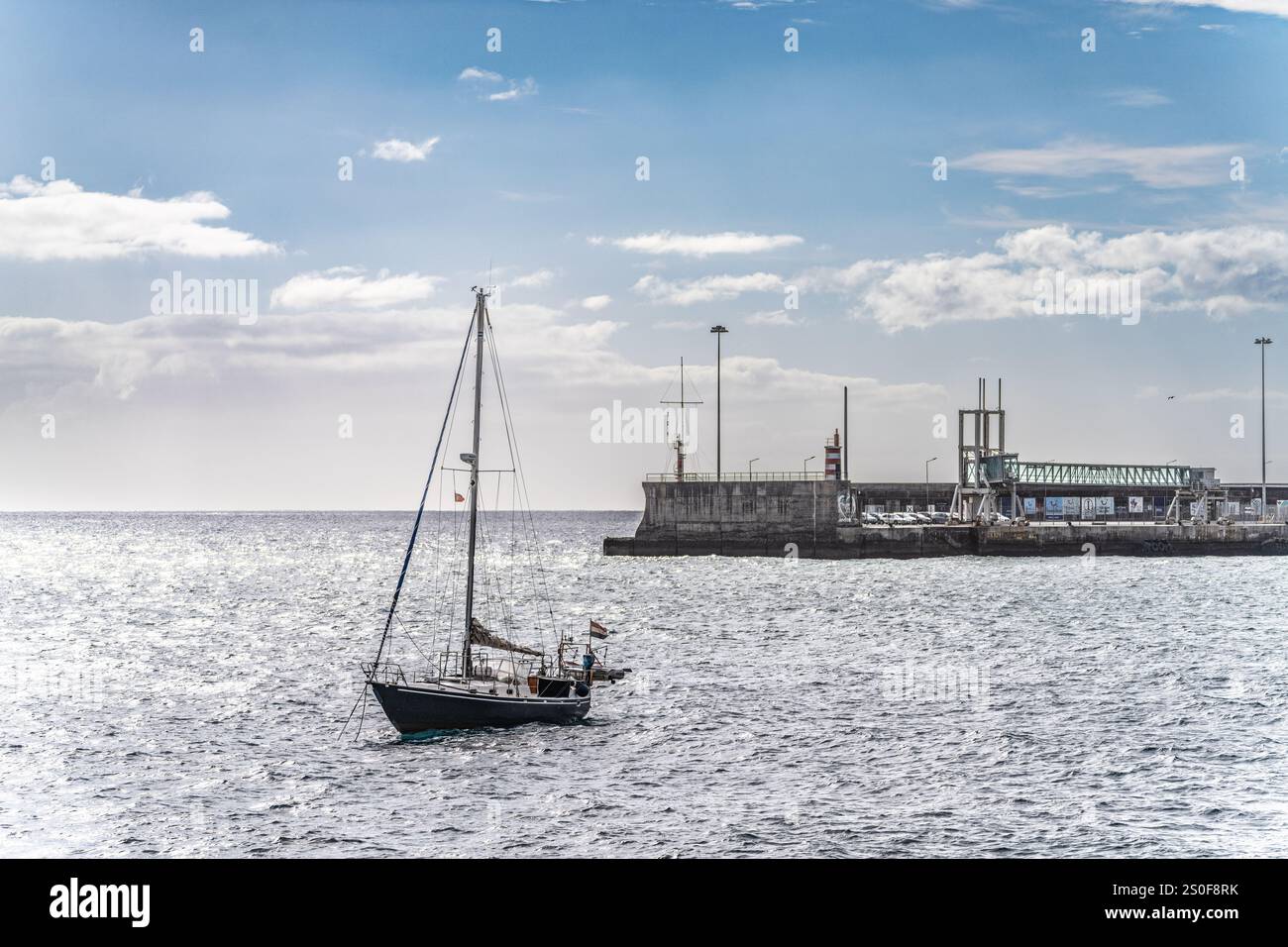 Barca a vela che galleggia vicino a un tranquillo porto sotto un cielo soleggiato, evidenziando la tranquillità marittima e il tempo libero. Foto Stock