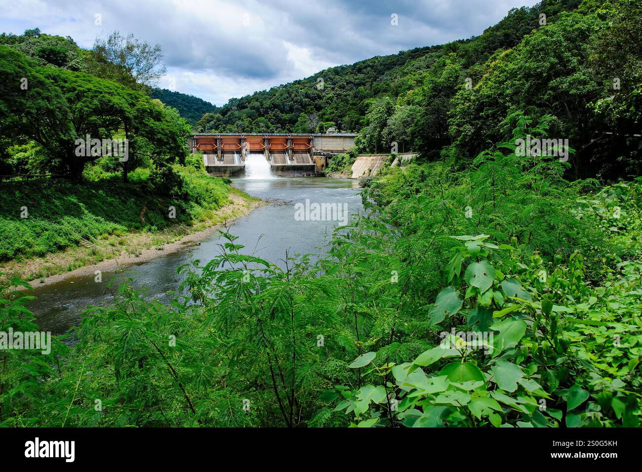 i cancelli della diga si aprono, rilasciando acqua nel fiume sottostante. L'acqua è di colore marrone fangoso, probabilmente a causa dei sedimenti trasportati dal fiume. TH Foto Stock
