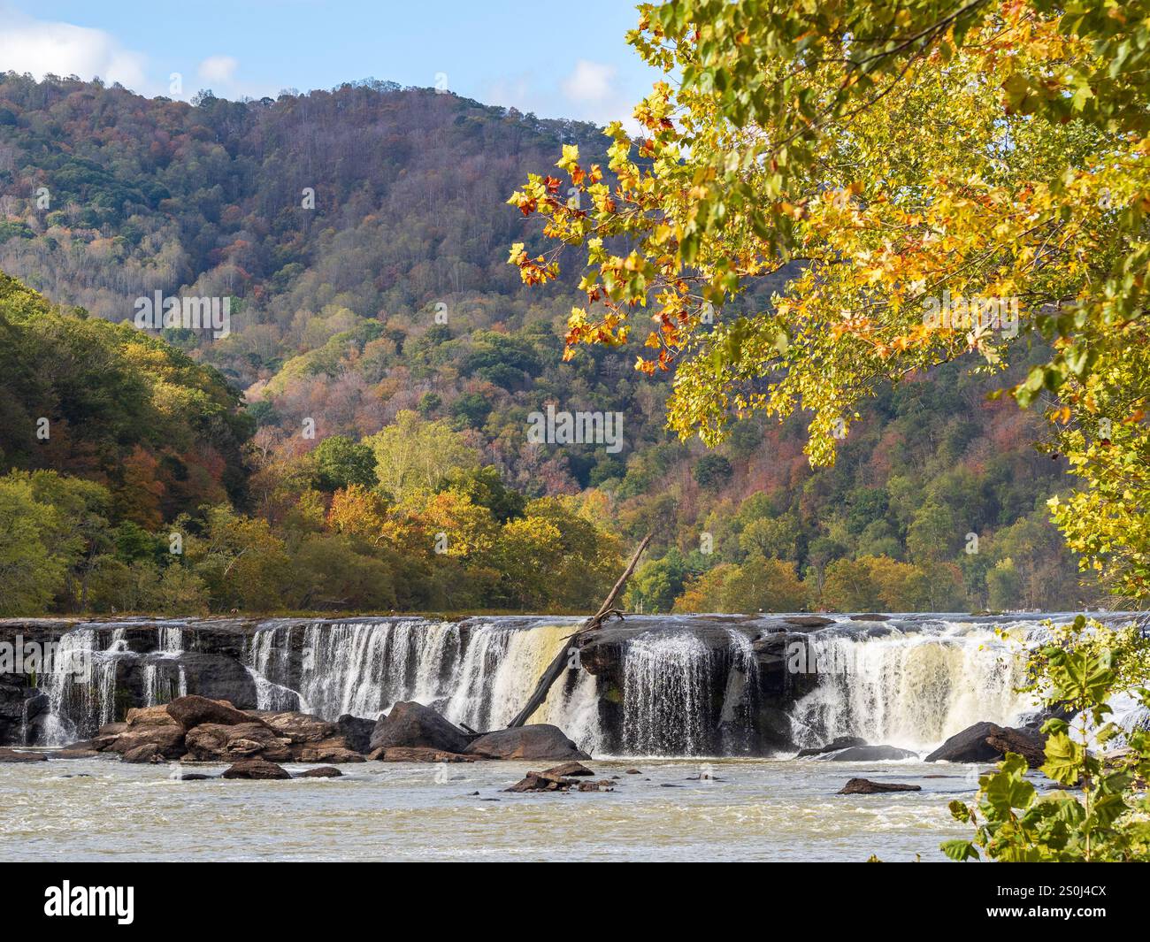 Le cascate Sandstone Falls, il New River Gorge National Park, West Virginia, si affacciano su brillanti colori autunnali sotto un cielo azzurro vivace, mentre i raggi del sole fanno il bagno Foto Stock