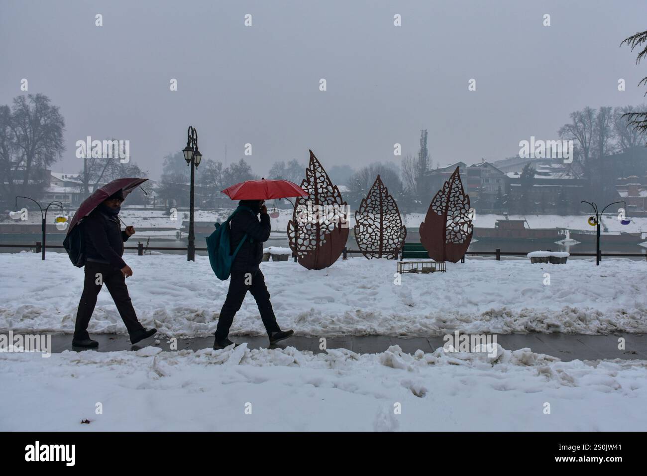 I turisti indiani tengono gli ombrelli mentre camminano lungo la strada innevata durante le nevicate a Srinagar, la capitale estiva del Jammu e del Kashmir. Le forti nevicate hanno gravemente interrotto la vita normale in tutto il Kashmir, influenzando i viaggi, l'alimentazione elettrica e le infrastrutture. Con circa 17 pollici di neve registrati in alcune aree, l'autostrada Jammu-Srinagar e i servizi ferroviari rimangono sospesi. Foto Stock